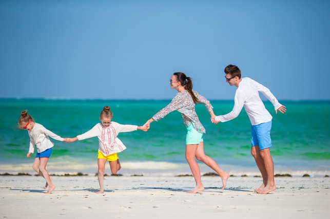 Family enjoying a beach day during spring break, playing together on the sand by the turquoise water, emphasizing fun and relaxation.