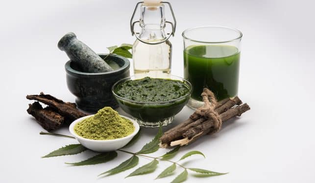 Green herbal ingredients for oral health, including a mortar and pestle, bowls of green paste and powder, a glass of liquid, and neem leaves, reflecting the evolution of toothpaste and natural dental care.